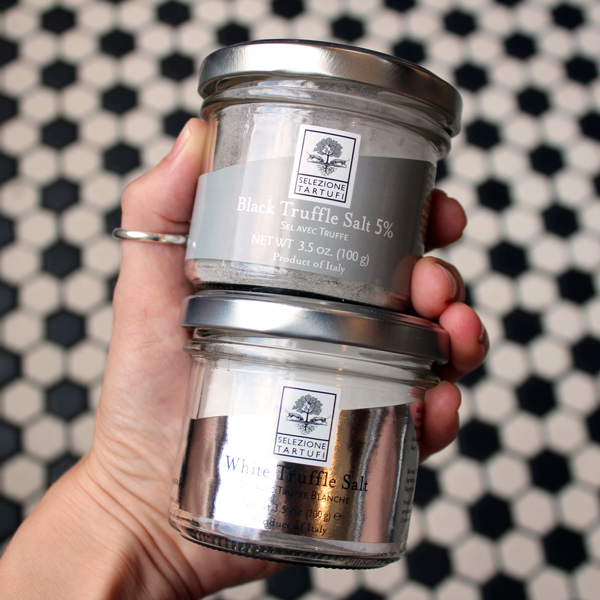 Black and White truffle salt jars being held in someone's hand with Deli tile in the background