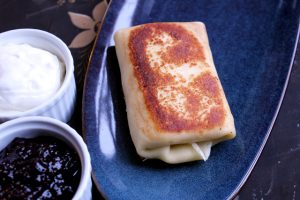 Zingerman's Cheese Blintz (crêpes) on a blue plate with sourcream and berry preserves