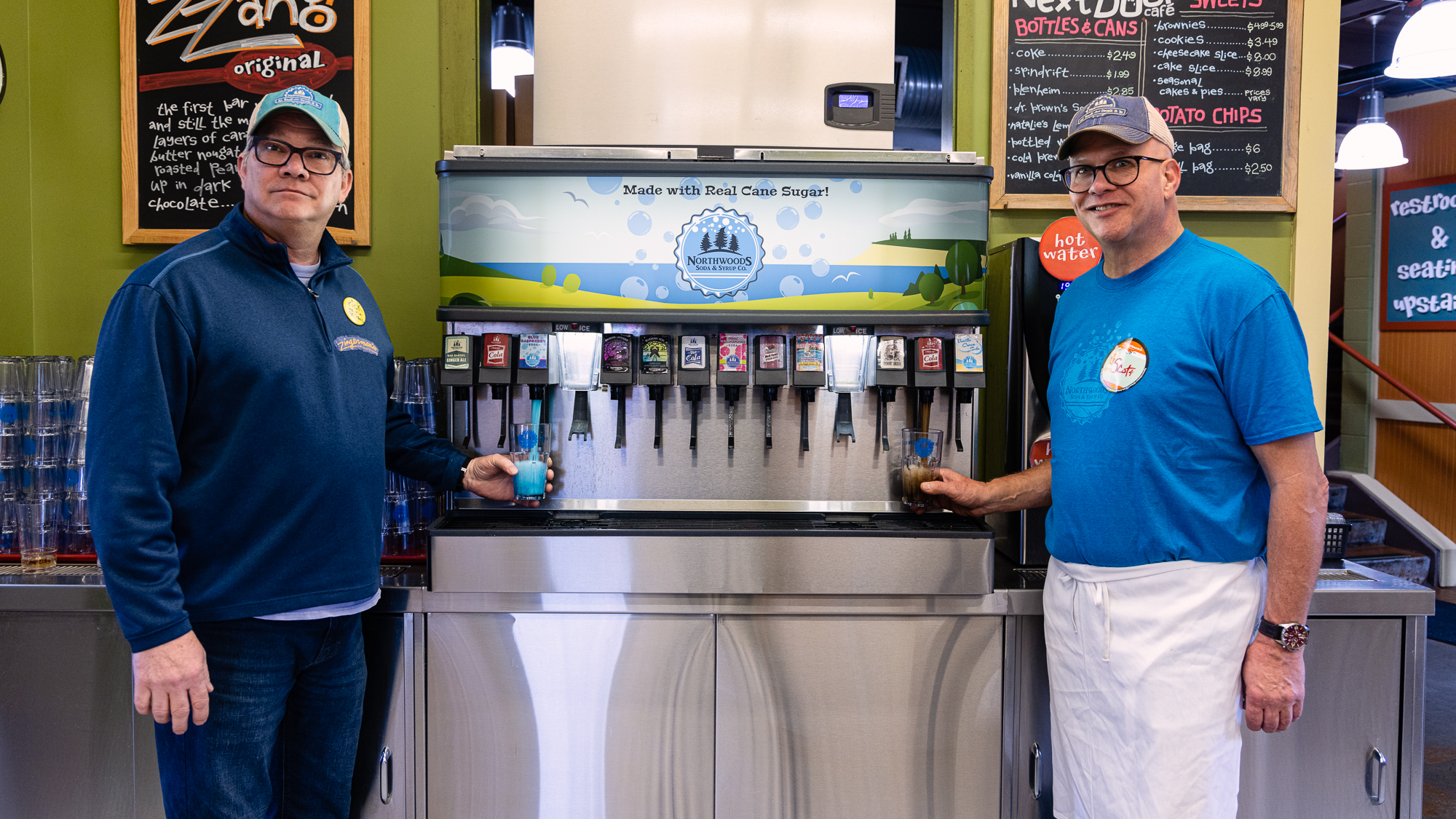 a photo of Deli managing partner Rick Strutz and Deli staffer Scott Geisler standing on either side of the soda fountain with the Northwoods logo and tap stickers