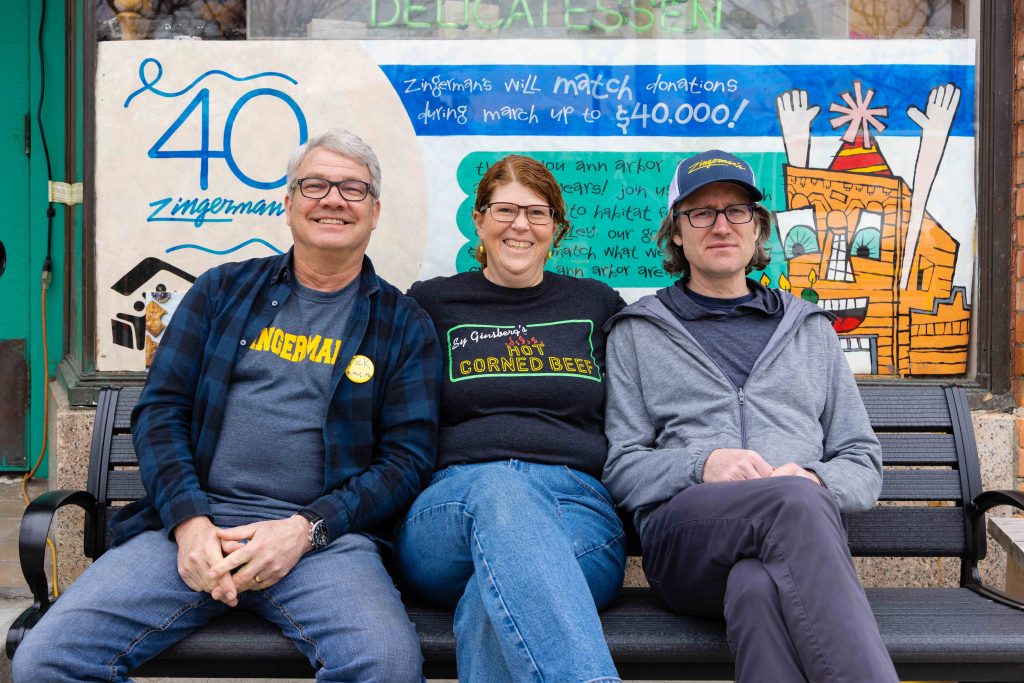 a photo of Deli Managing Partners Rick Strutz, Grace Singleton and Rodger Bowser sitting on the bench in front of the Deli