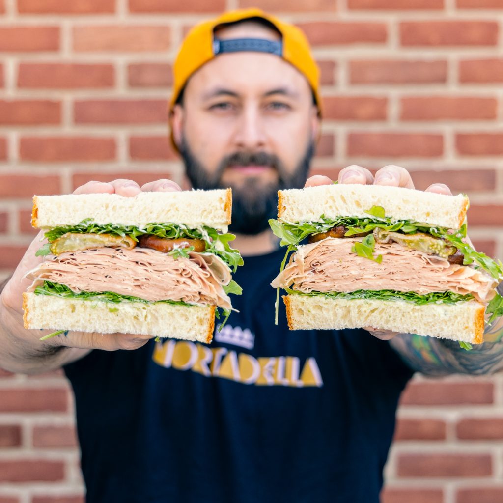 a photo of our Sandwich Line Manager Mike V holding a half sandwich in each hand