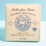 Patience Gray’s Preferred Breakfast A box of Bellwether Farms Basket Ricotta. The box is a light tan with a blue illustration of a cow on a mountain in front of some clouds.