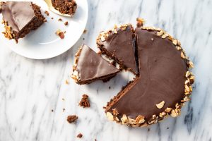 A top-down photo of a Flourless Chocolate Orange Torte on a marble countertop with two slices cut from it, and another slice on a circular white plate along with a fork.