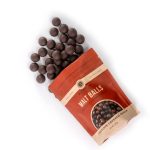 Artisanal Malt Balls from Askinosie A photo of a bag of Askinosie Malt Balls on a white surface with many malt balls pouring out. The bag is a deep matte orange.