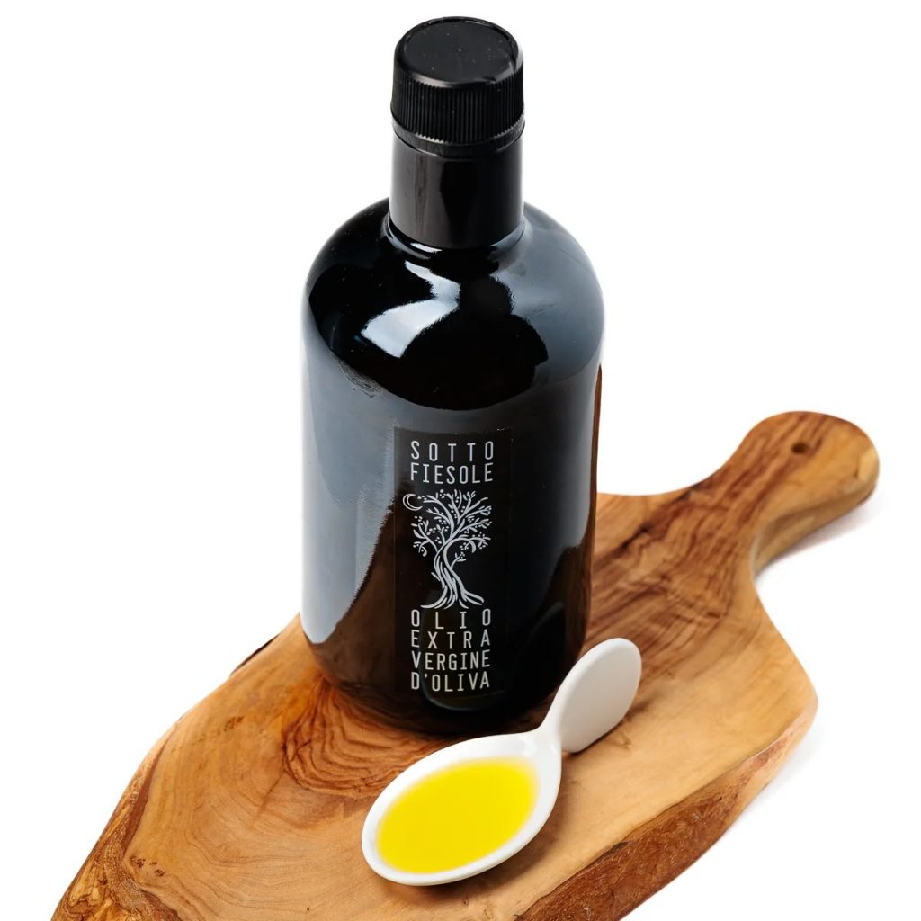 A photo of a bottle of Sotto Fiesole on a wooden serving board with a white tasting spoon holding some of the olive oil.