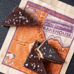 Nanaimo Bars from Zingerman's Bakehouse A top-down photo of three triangular Nanaimo Bars, one of which has a bite taken from it, resting on a Bakehouse pastry bag.