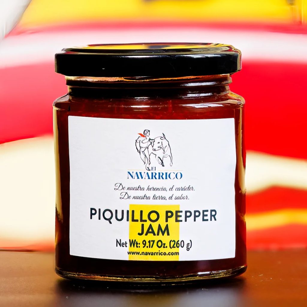 A photo of a glass jar of El Navarrico Piquillo pepper jam. The jar is short with a white label and black text with a yellow rectangle accent.