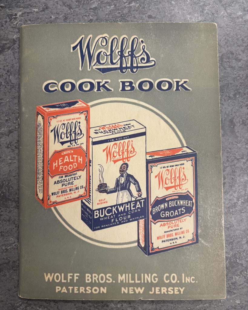 A photo of Wolff's Cook Book, featuring illustrations of boxes of Wolff's Health Food, Buckwheat, and Brown Buckwheat Groats. 