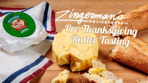 A photo of a round of Beurre de Baratte butter on a wooden surface, with a torn baguette on the right and the butter's parchment wrapper to the left, and overlaid text that reads "Zingerman's Delicatessen Pre-Thanksgiving Butter Tasting."