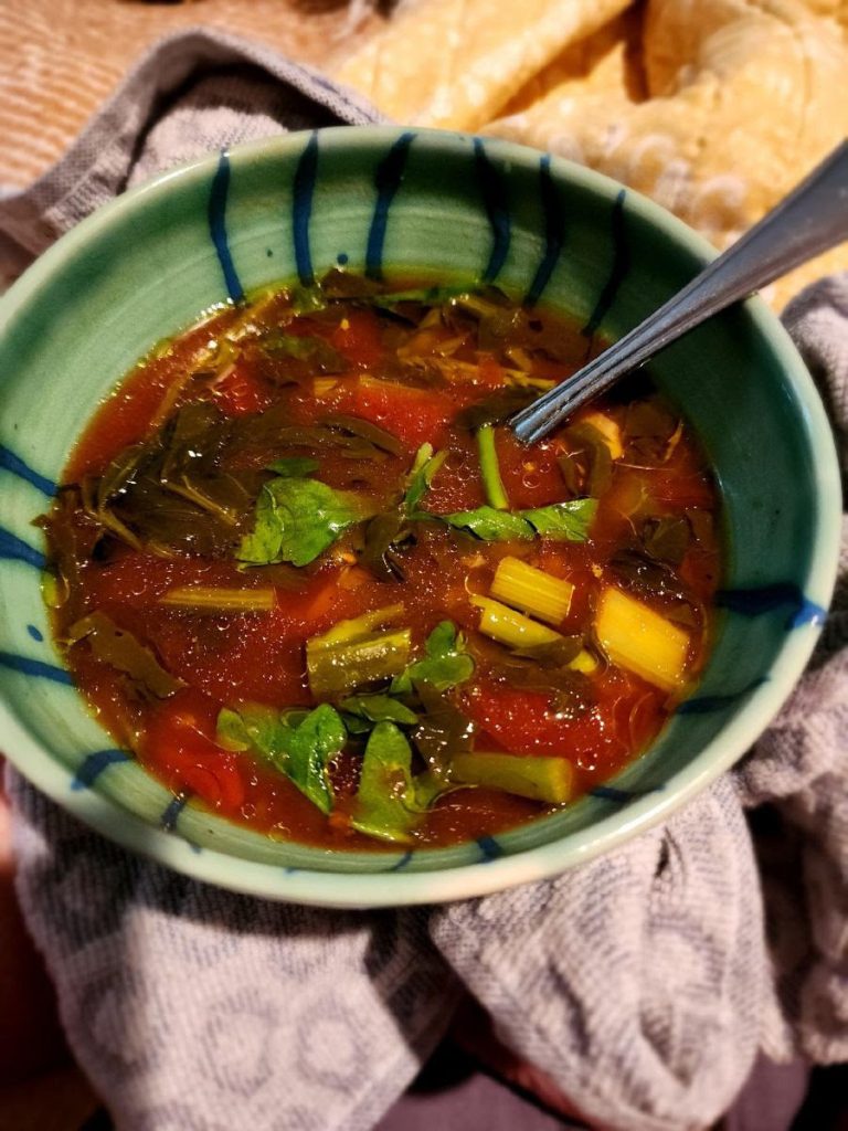 A photo of a ceramic bowl of Fresh Spring Vegetable Soup with a spoon resting in the bowl.