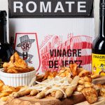 A photo of both bottles of Sanchez Romate sherry vinegar on either side of a cheeseboard, with a box of Sanchez Romate vinegar behind it.