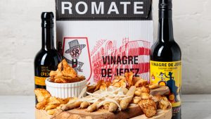 A photo of both bottles of Sanchez Romate sherry vinegar on either side of a cheeseboard, with a box of Sanchez Romate vinegar behind it.