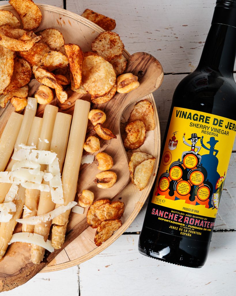 A top-down photo of a bottle of Sanchez Romate Sherry Vinegar next to a cheeseboard.