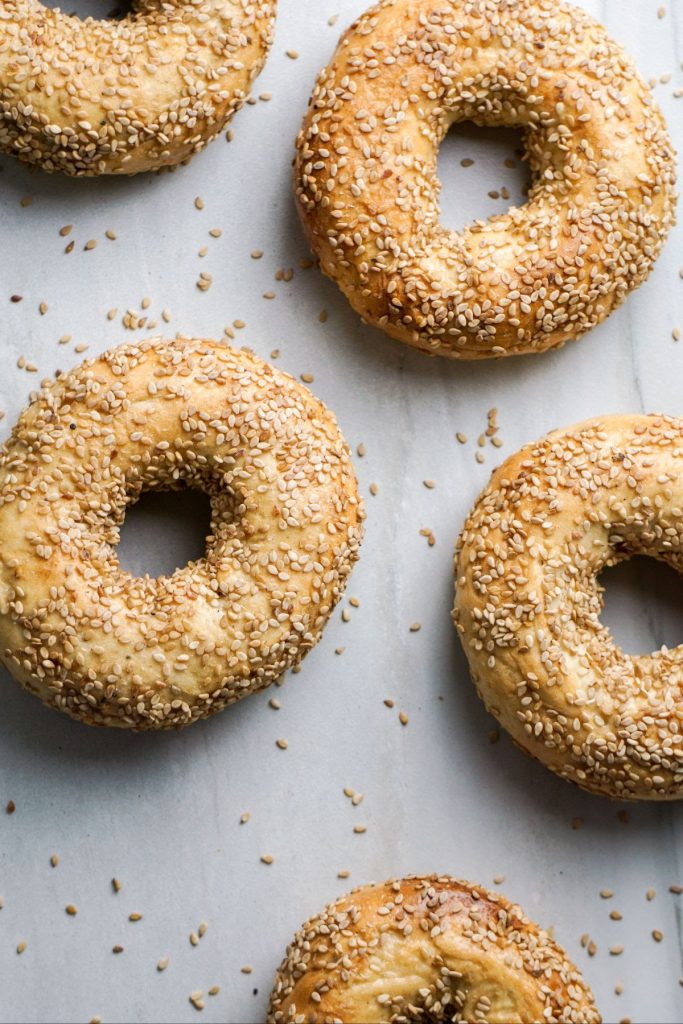 A top-down photo of several Sesame bagels on a light gray surface.
