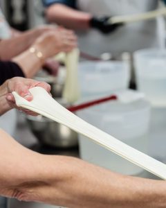 A photo of a set of hands stretching mozzarella at a work table.