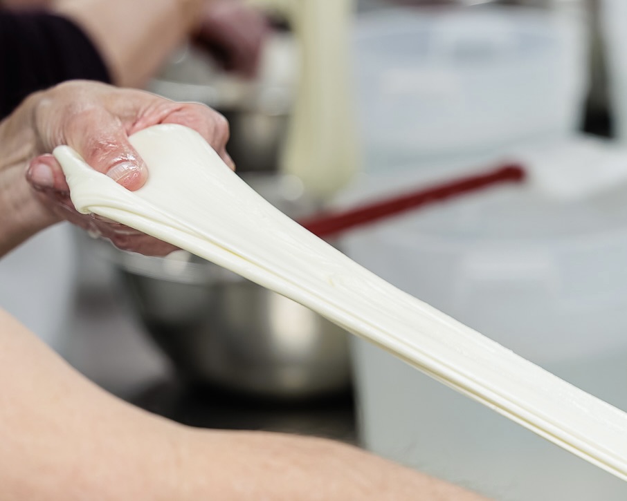 A photo of a set of hands stretching mozzarella. 