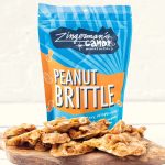 Traditional Handcrafted Peanut Brittle from the Candy Manufactory A photo of a bag of Zingerman's Candy Manufactory Peanut Brittle, with pieces of brittle resting in front of the bag.