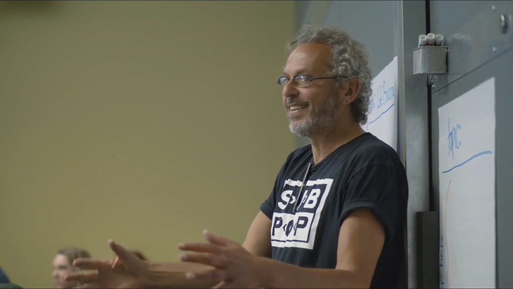 A photo of Ari standing in front of a whiteboard, teaching a class.