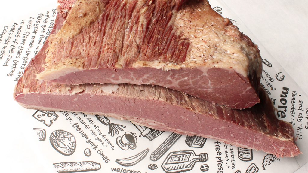 A photo of two slabs of corned beef on a sheet of Deli paper.