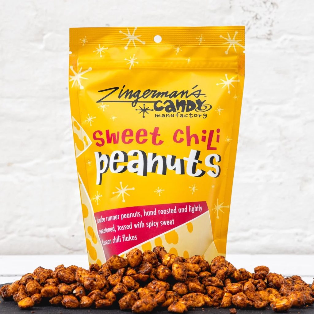 A photo of a bag of the Candy Manufactory's Sweet Chili Peanuts, with a pile of the peanuts in front of the bag.