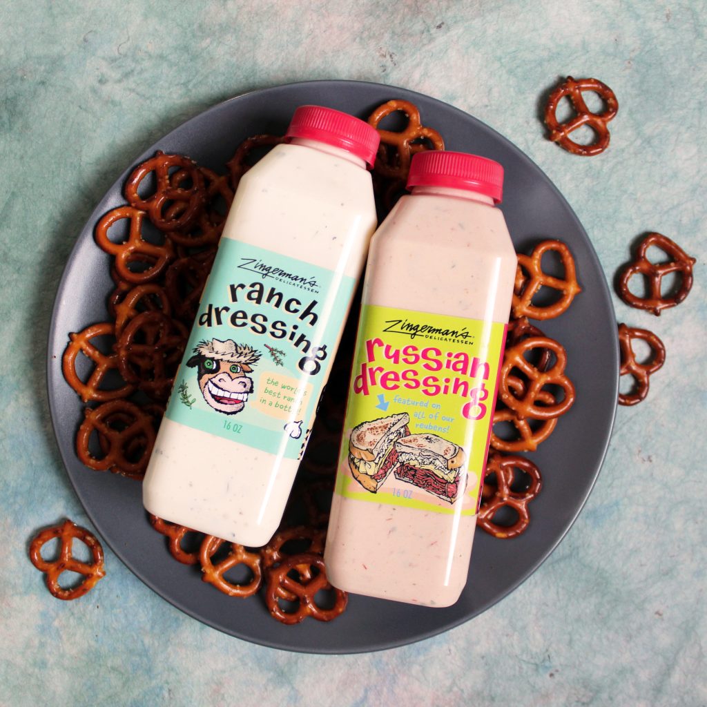 A top-down photo of a bottle each of Russian and Ranch Dressing resting on a plate with pretzel twists.