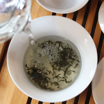 A top-down photo of water being poured over a cup of tea leaves.