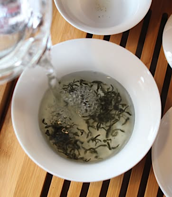 A top-down photo of water being poured over a cup of tea leaves.