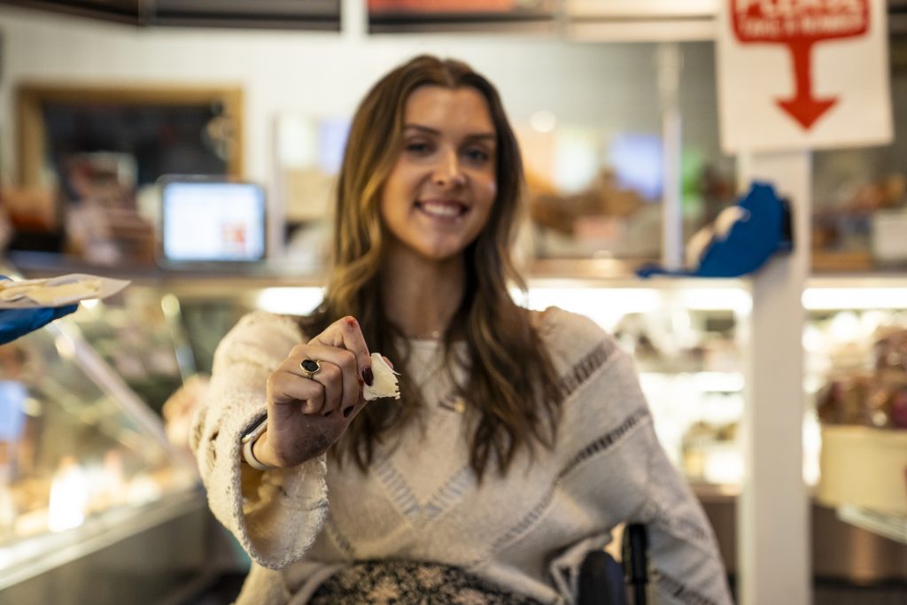 A photo of a woman in a wheelchair holding out a ticket from the number roll in the Specialty Foods department.