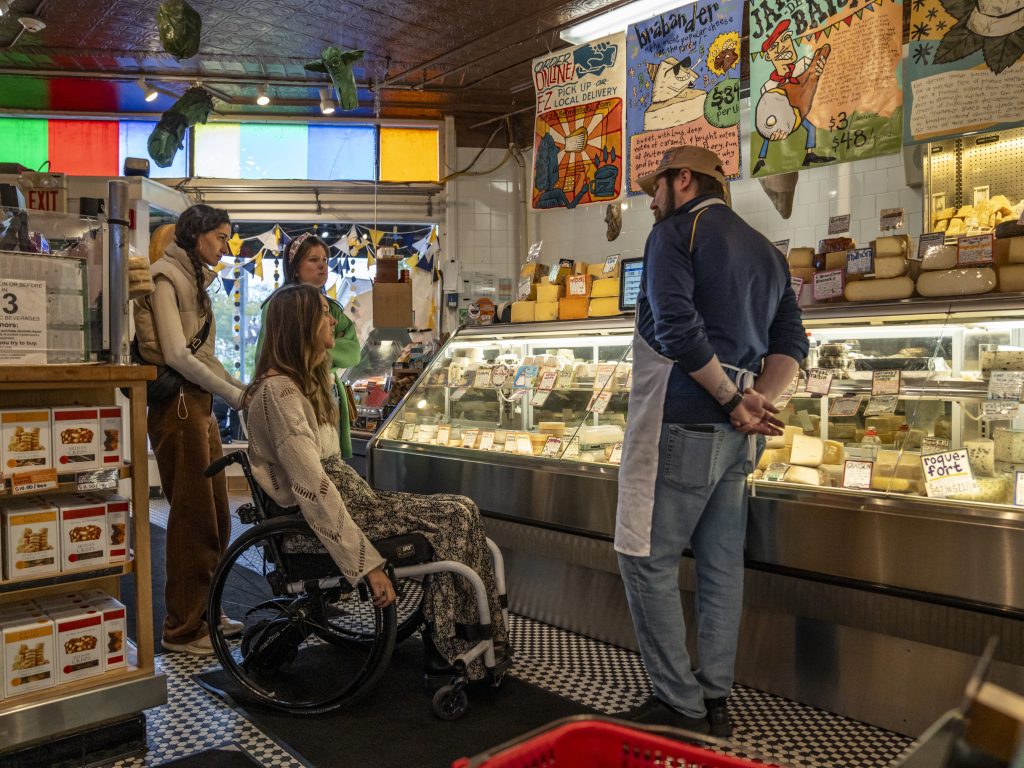 A photo of three women, one of whom is in a wheelchair, chatting with our fish buyer Kevin in front of the cheese counter.