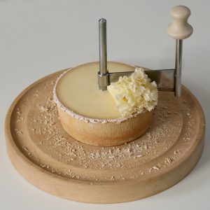 A photo of half a wheel of Tête de Moine positioned on a girolle, with a florette resting atop the wheel.