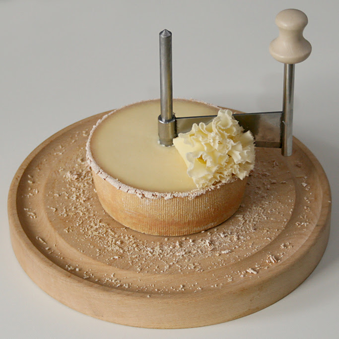 A photo of half a wheel of Tête de Moine positioned on a girolle, with a florette resting atop the wheel. 