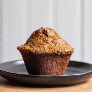 A photo of a pumpkin muffin on a black ceramic plate.