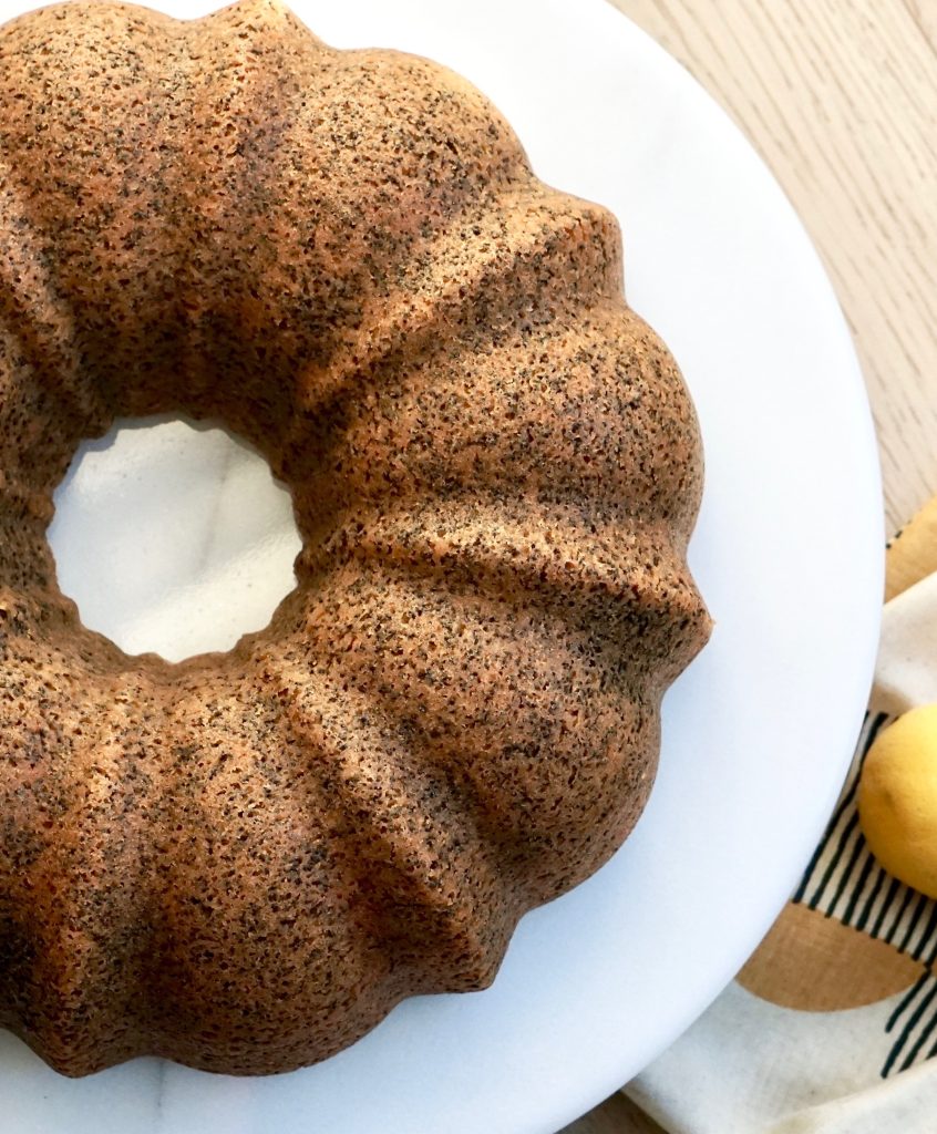 A top-down photo of a Lemon Poppyseed Coffee Cake on a circular white cake stand.