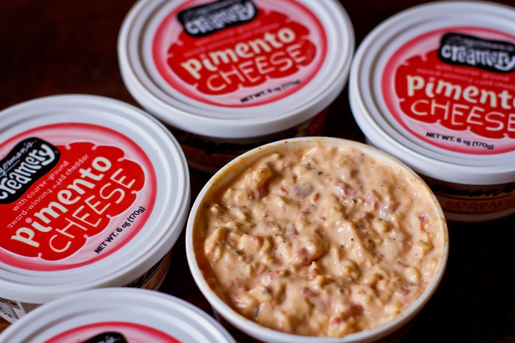 A photo of several containers of Zingerman's Pimento Cheese, one of which is opened to show the dip inside.